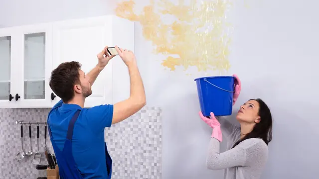 Homeowner photographing a water-stained wall while another person holds a bucket