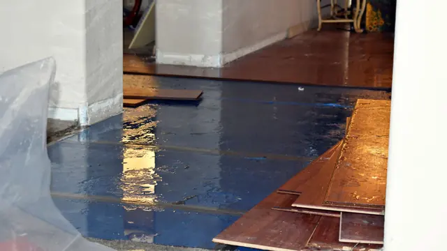 Wood floor planks lifted from a wet subfloor with plastic sheeting along the wall